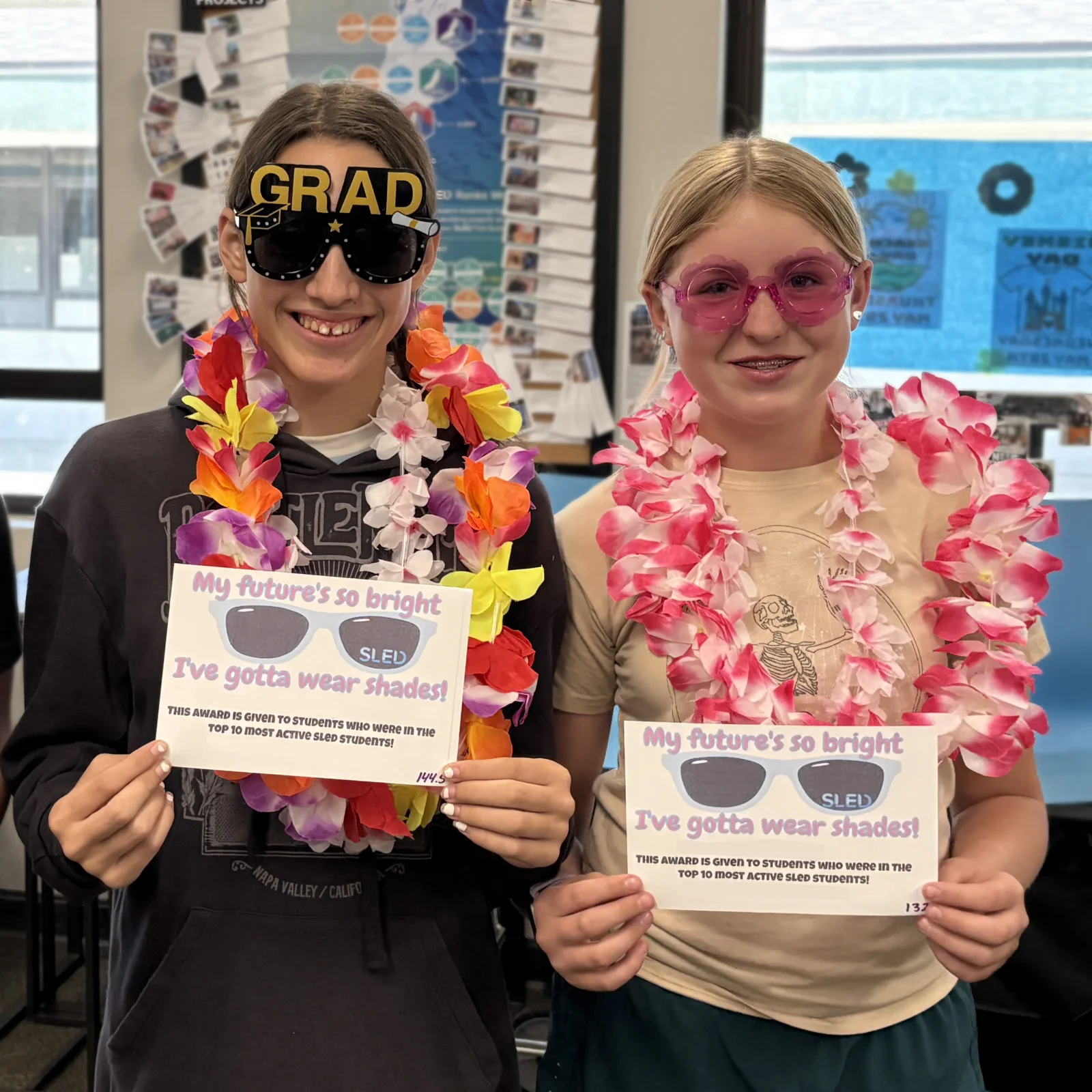 Two students in leis and novelty sunglasses hold up their SLED awards